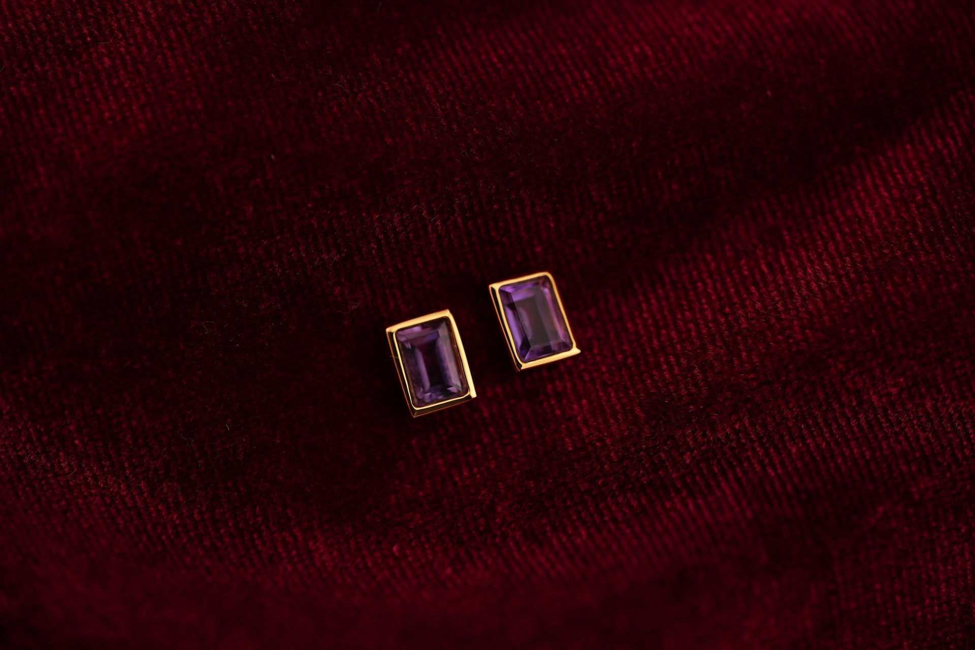Pair of gold earrings with purple gemstones on a burgundy fabric background