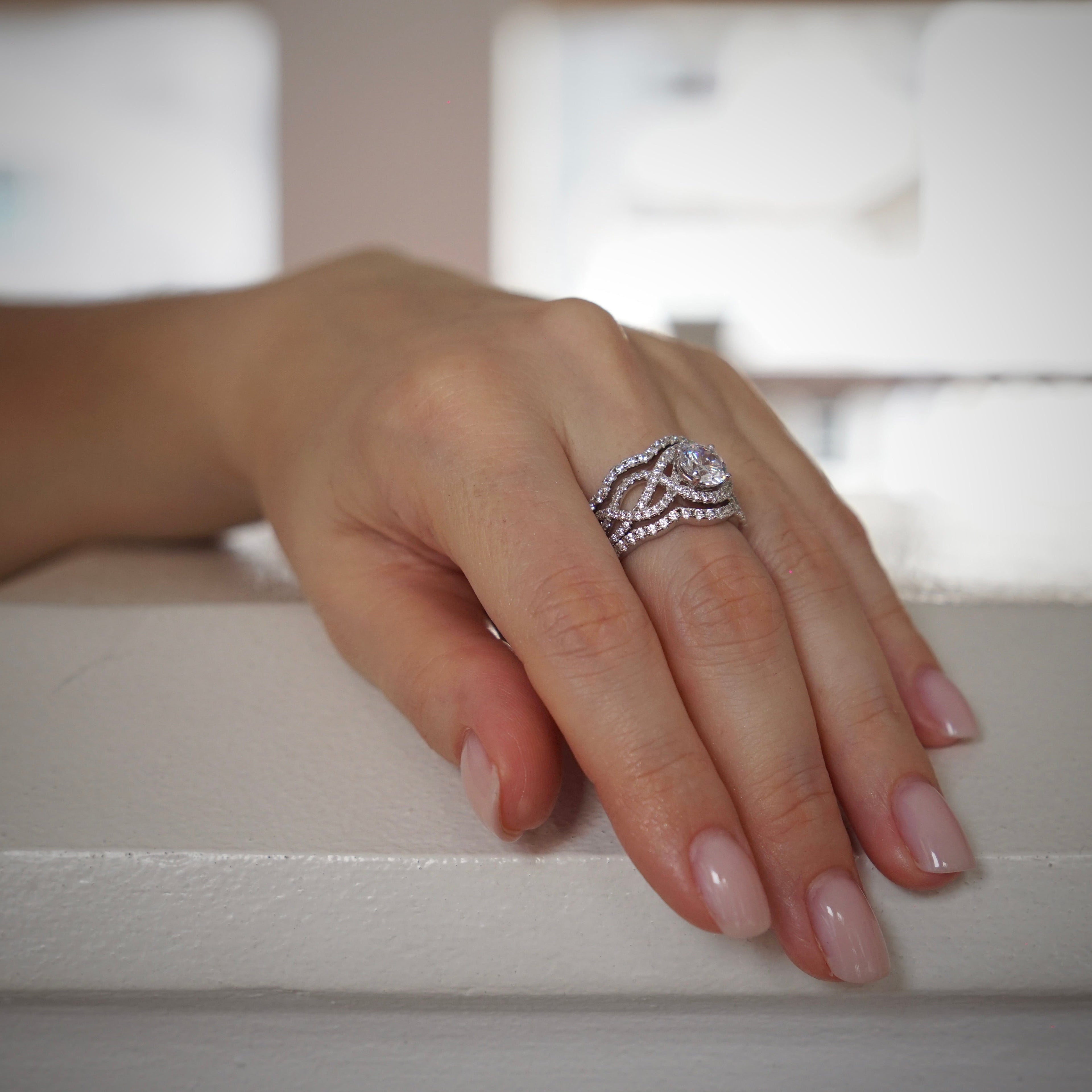 Hand wearing a silver ring on a white surface with a blurred background
