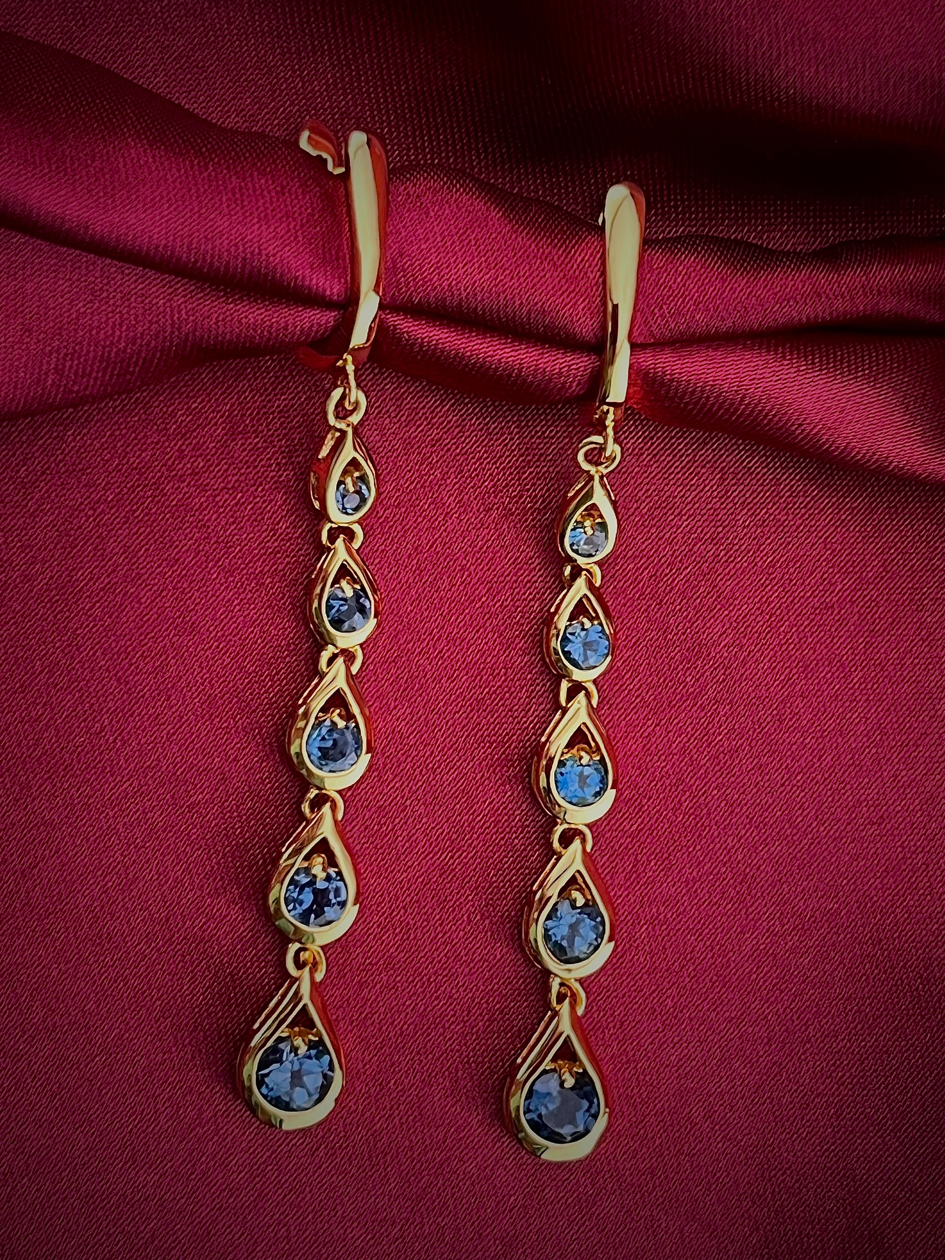 Haspiera blue cocktail dangle earrings with gold setting on burgundy fabric background