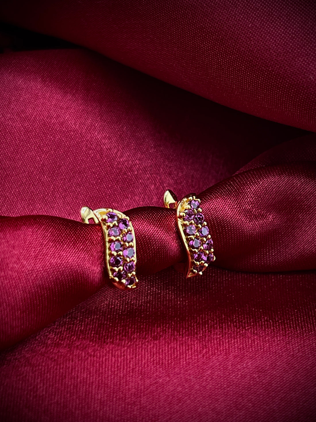 Haspiera berry leaf purple earrings with gold setting and purple gemstones on red fabric