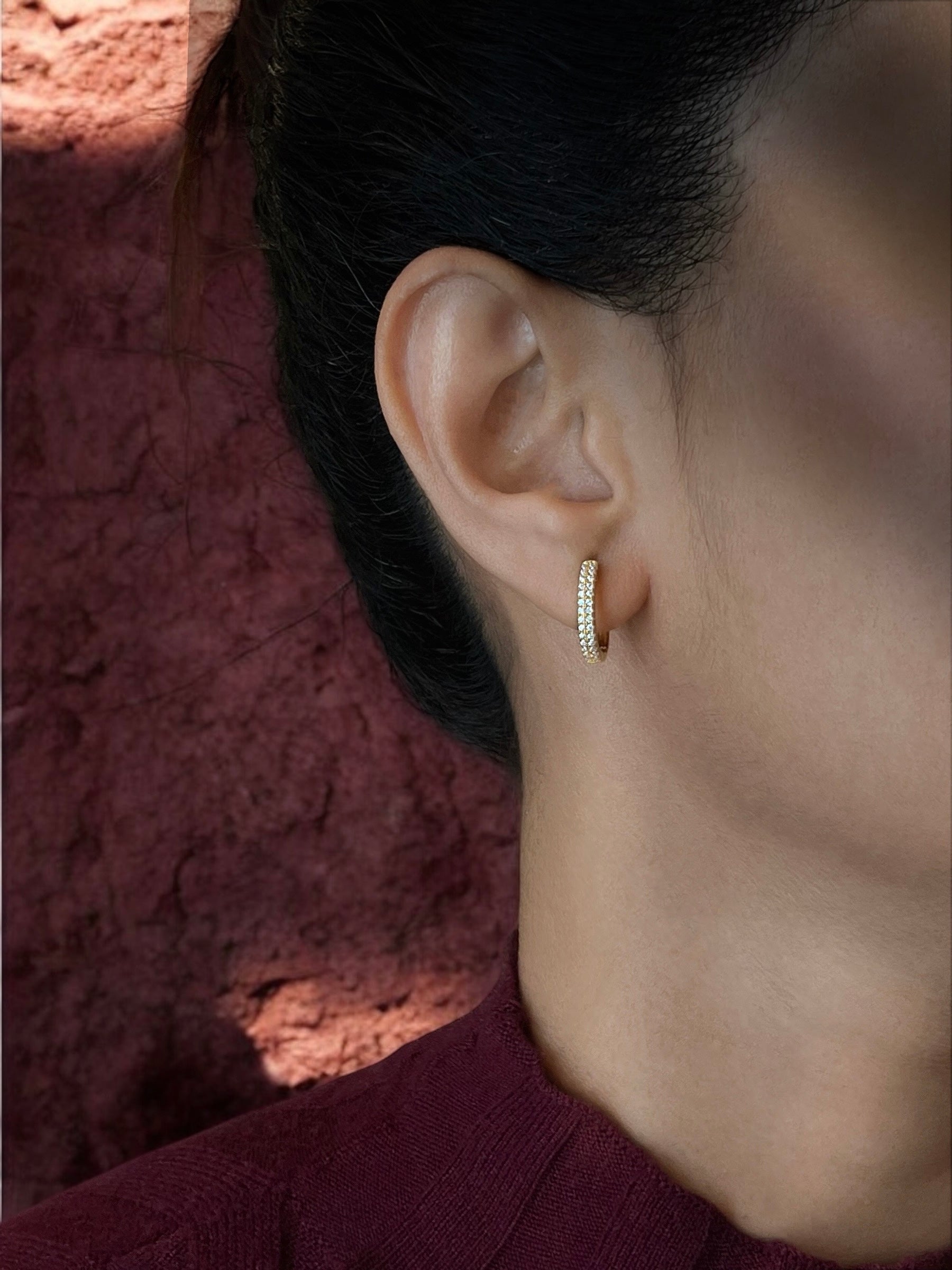 Haspiera pave crystal huggie earrings worn on ear with textured red background