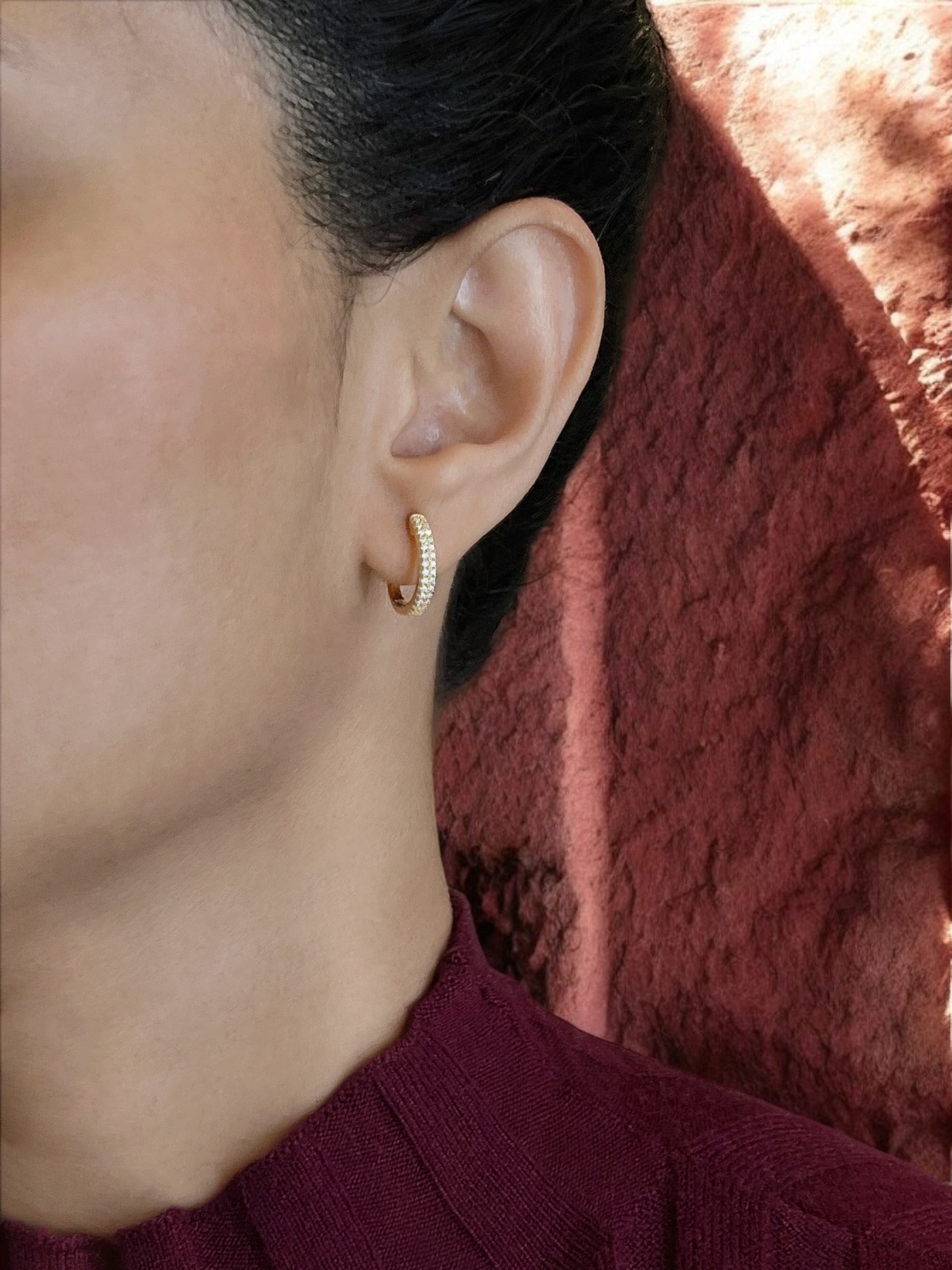 Haspiera pave crystal huggie earrings in gold worn on ear with textured background
