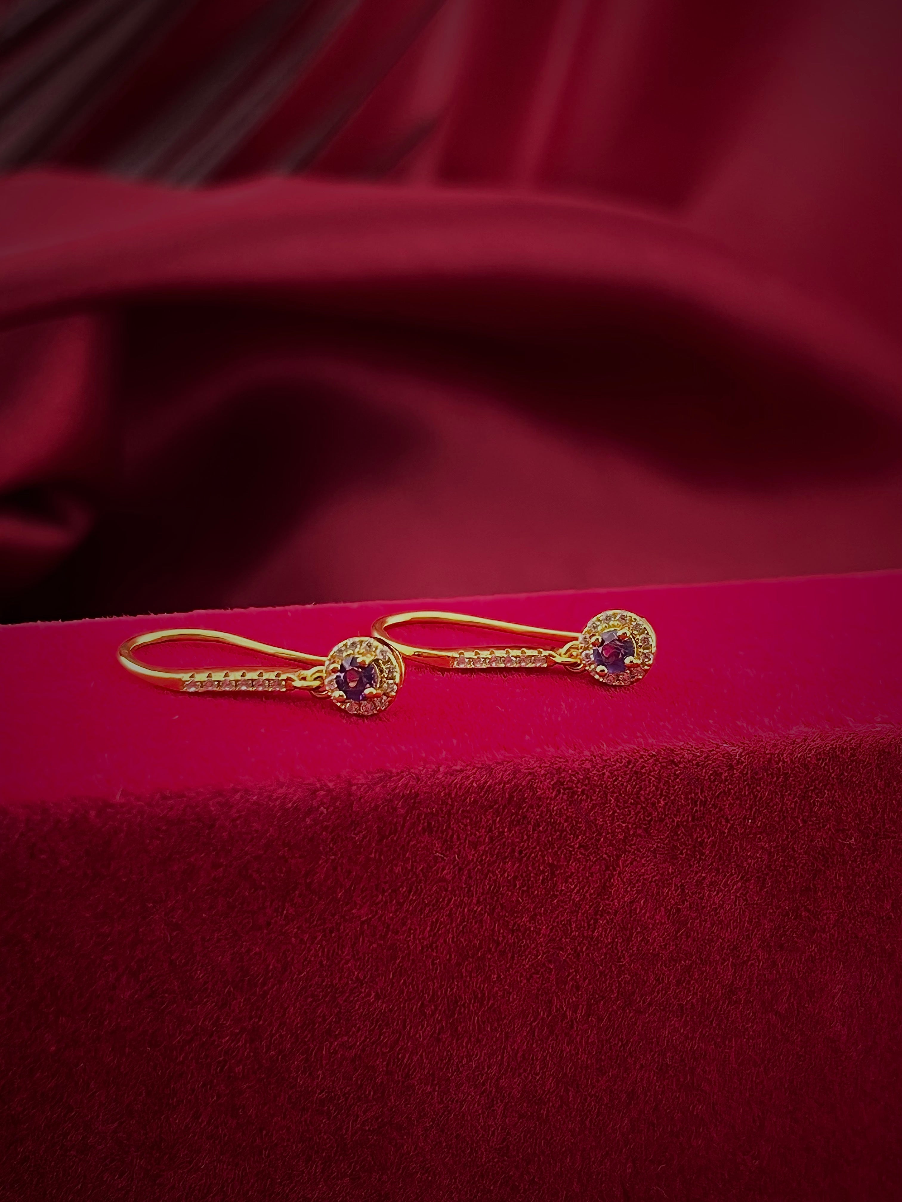 Haspiera gold gemstone violet drop earrings with intricate detailing on red velvet background