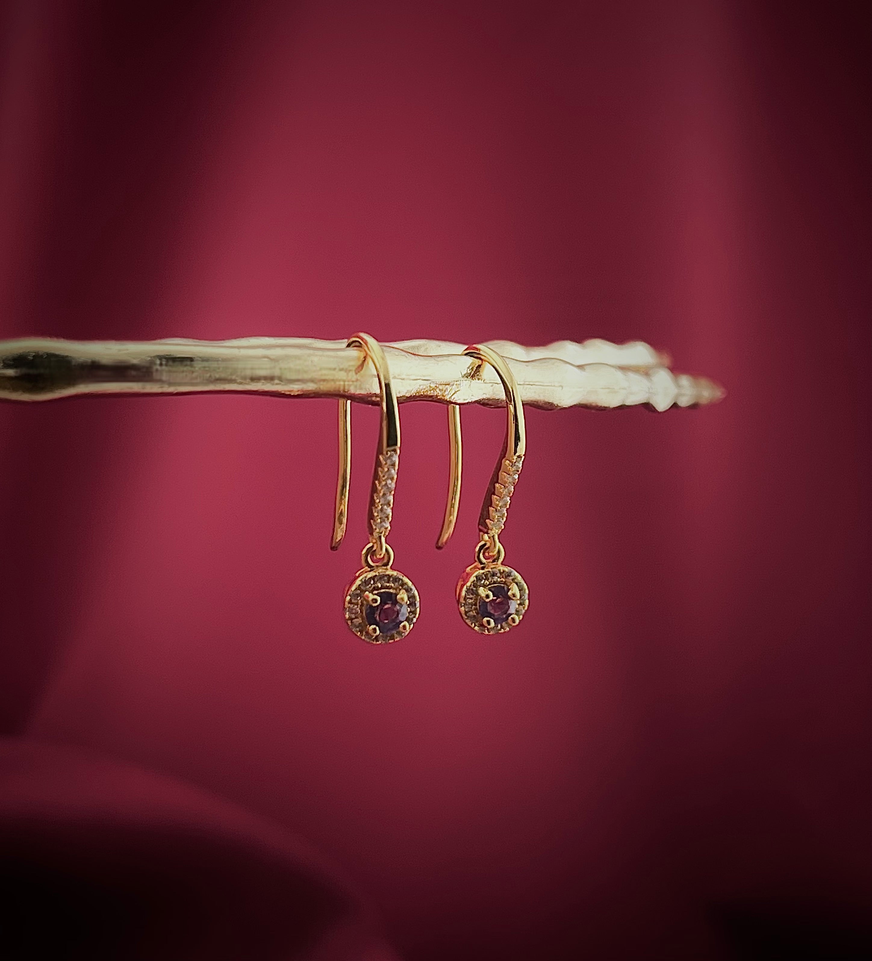 Haspiera delicate violet drop earrings with gold hooks and gemstone details hanging on a textured branch