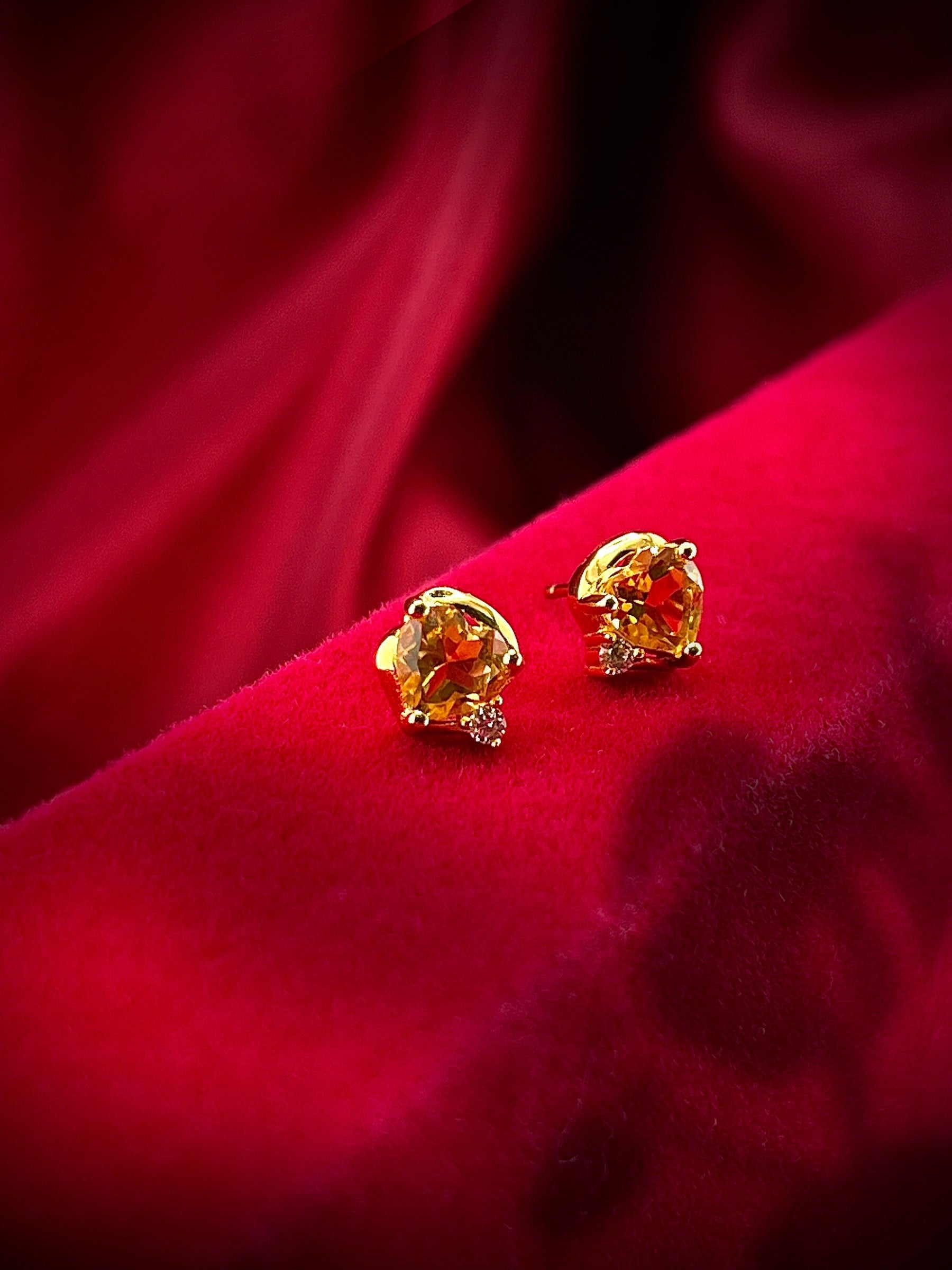Haspiera golden heart stud earrings with gemstone design displayed on red velvet fabric
