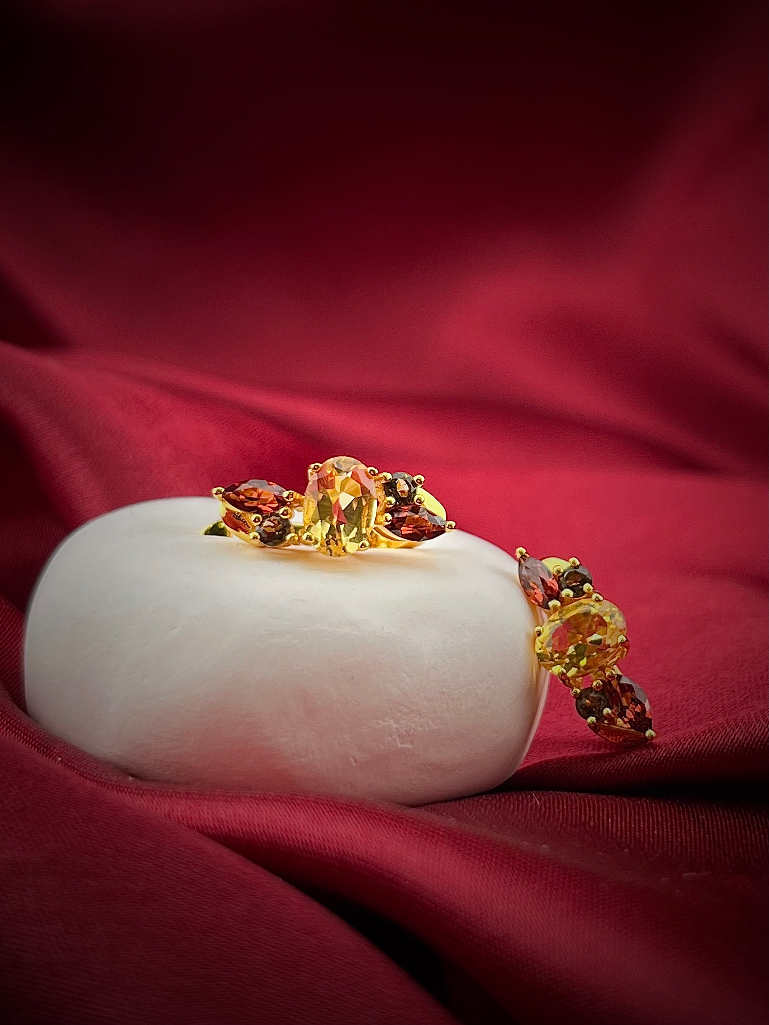 Haspiera harvest hues earrings featuring yellow and red gemstones set in gold on a white display with red fabric background