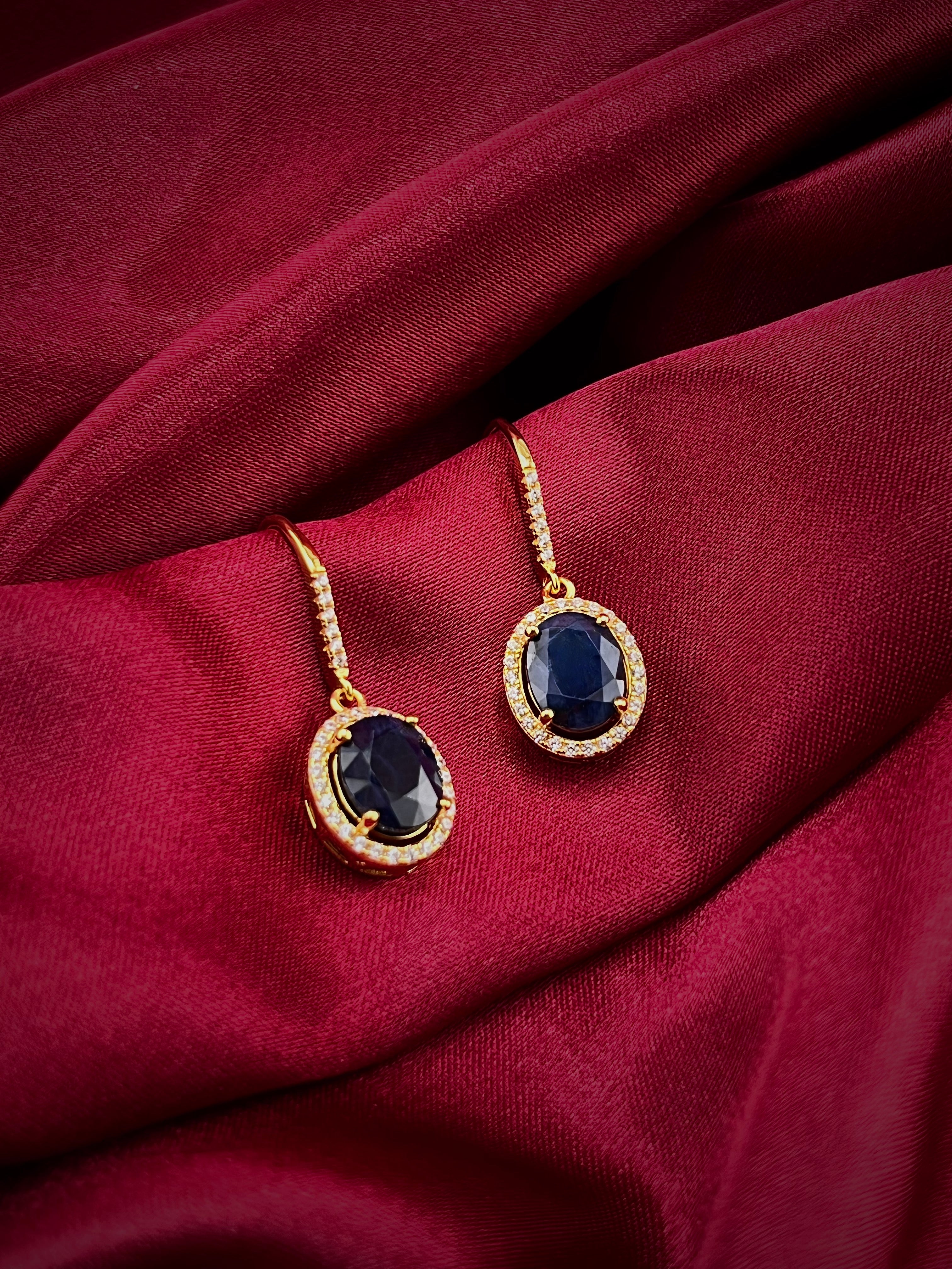 Haspiera sapphire drop earrings for women with gold setting and oval blue gemstones on red fabric