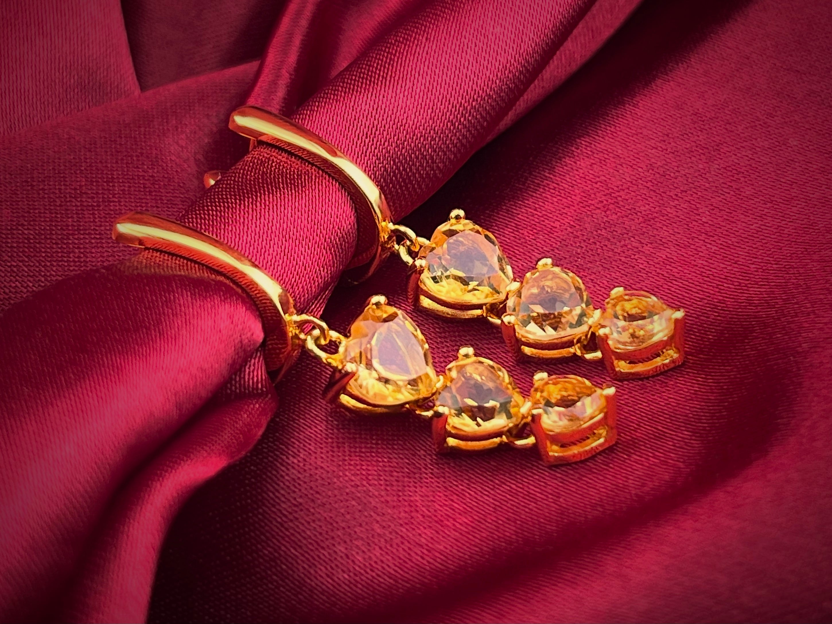 Haspiera yellow heart citrine dangle earrings with gold setting on red fabric background
