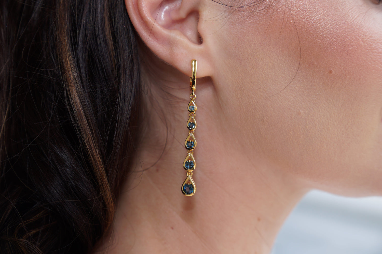 Gold earring with green gemstones worn by a person
