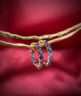 Haspiera amethyst hoop earrings with gold setting displayed on textured gold rods against a red background