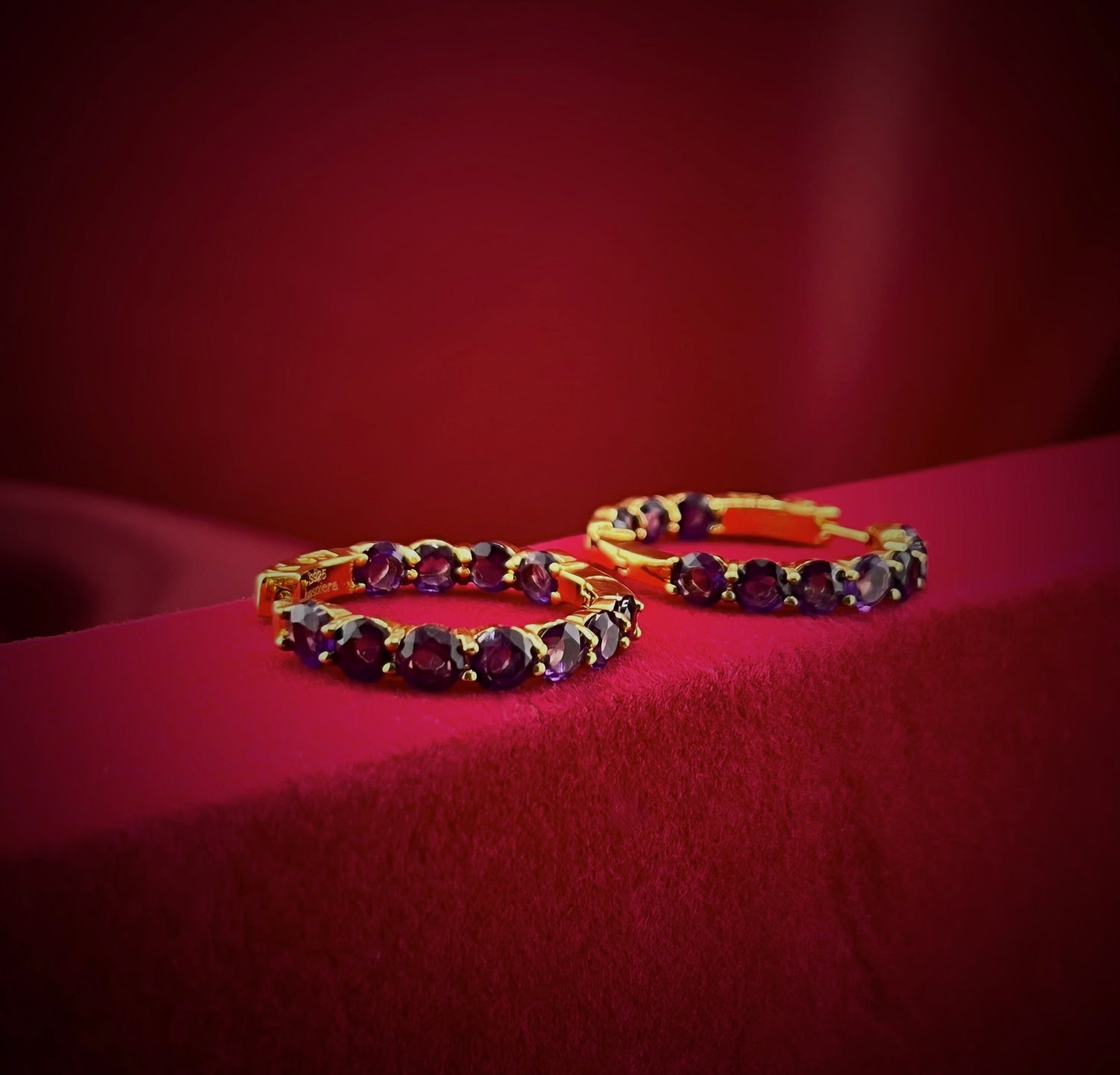 Haspiera amethyst hoop earrings with purple gemstones set in gold on red velvet background