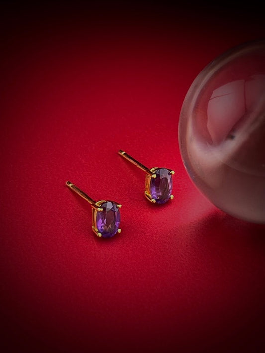 Haspiera amethyst stud earrings with oval purple gemstones set in gold on red background