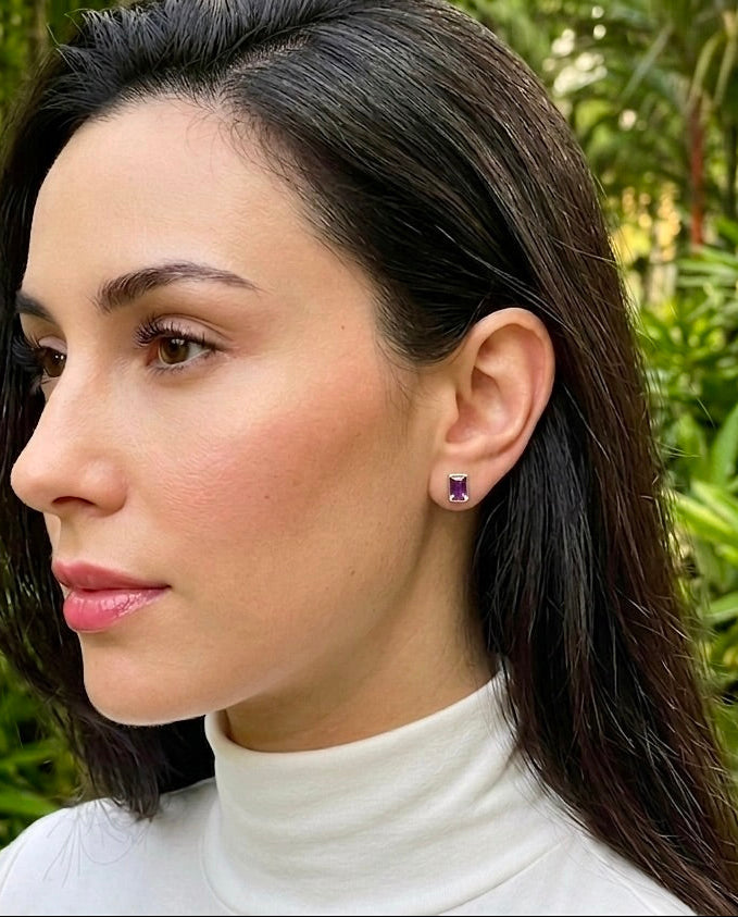 Woman wearing a white turtleneck with earrings against a green leafy background