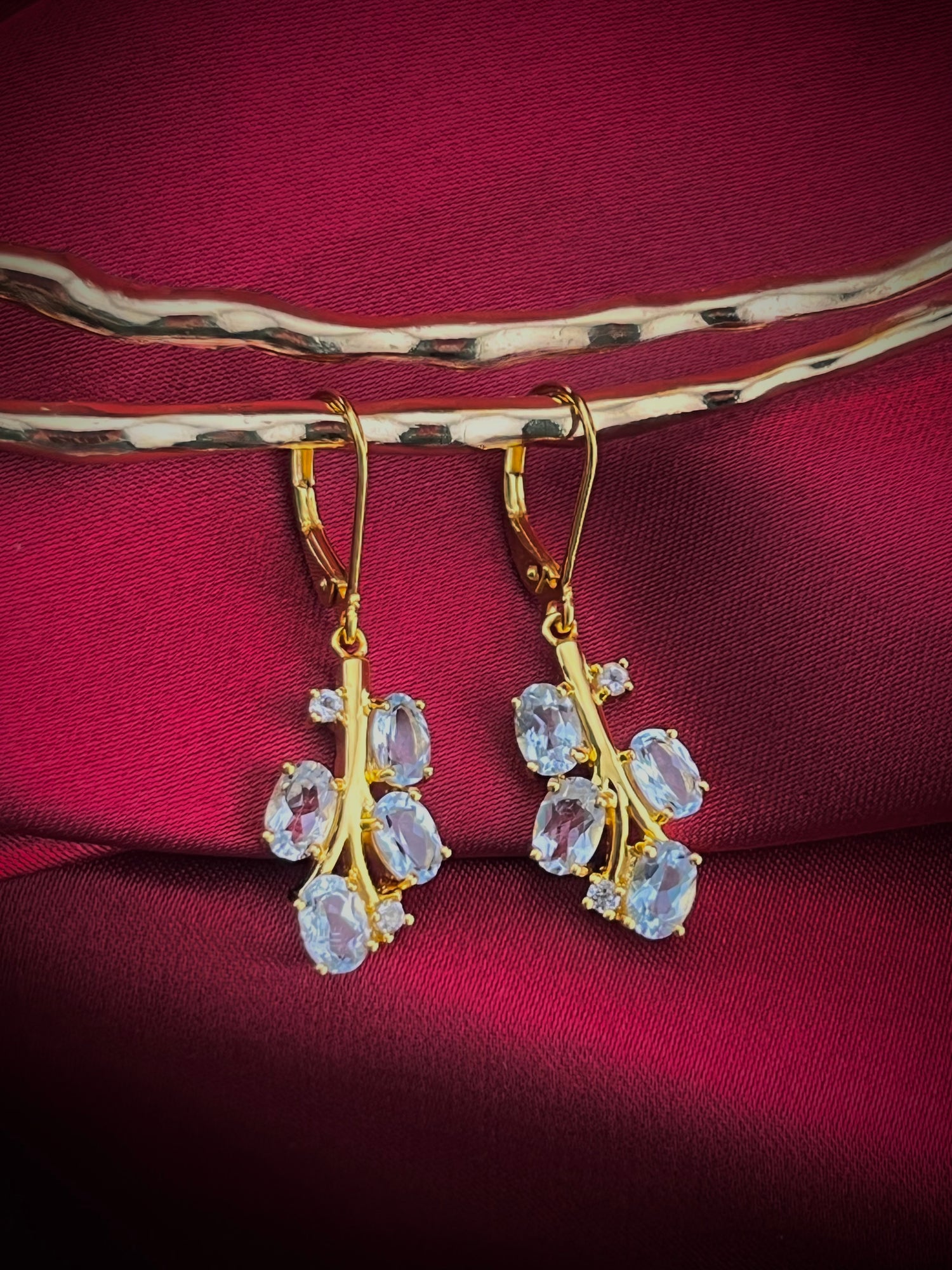 Haspiera blue leaf drop earrings featuring gold setting with oval blue gemstones on red fabric
