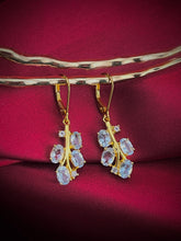 Haspiera blue leaf drop earrings featuring gold setting with oval blue gemstones on red fabric