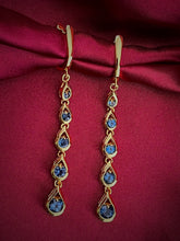 Haspiera blue cocktail dangle earrings with gold setting on burgundy fabric background