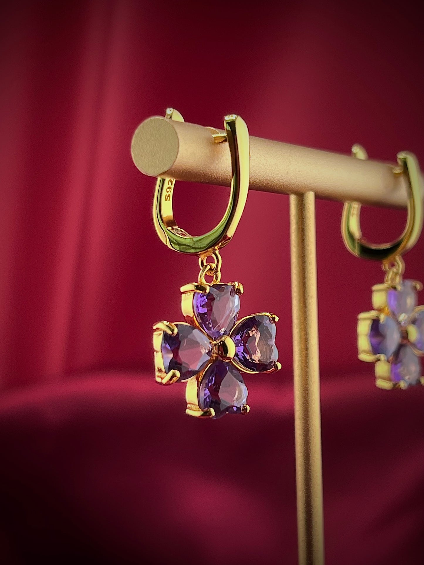 Haspiera four petal amethyst earrings with gold setting displayed on a stand against a red background