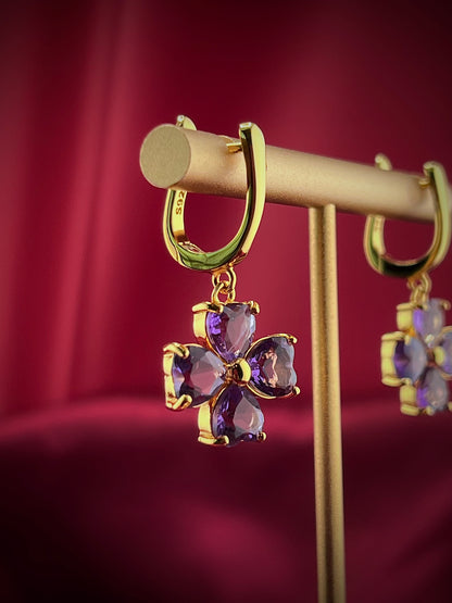 Haspiera four petal amethyst earrings with gold setting displayed on a stand against a red background