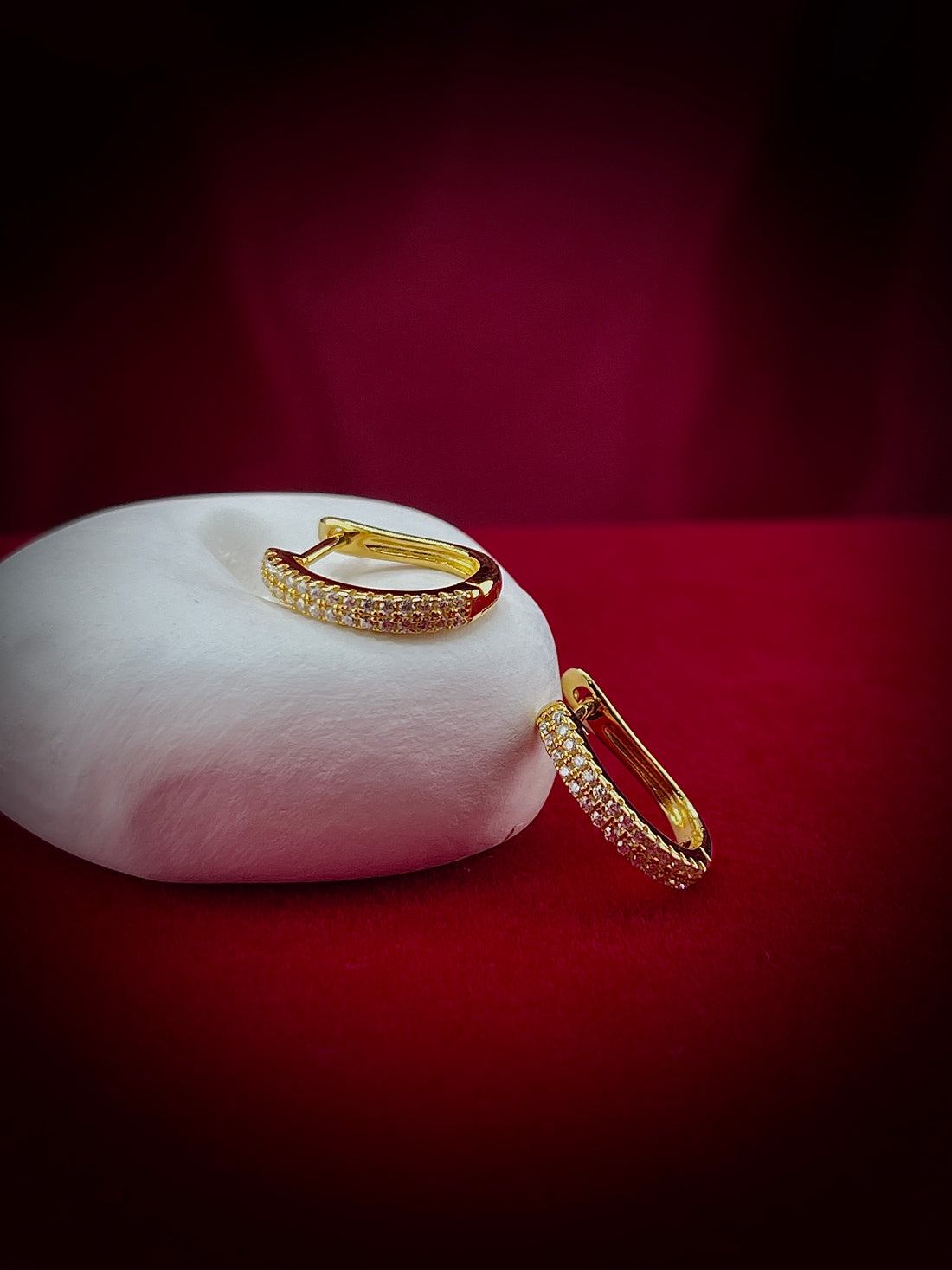Haspiera gold pave crystal huggie earrings displayed on white cushion with red background