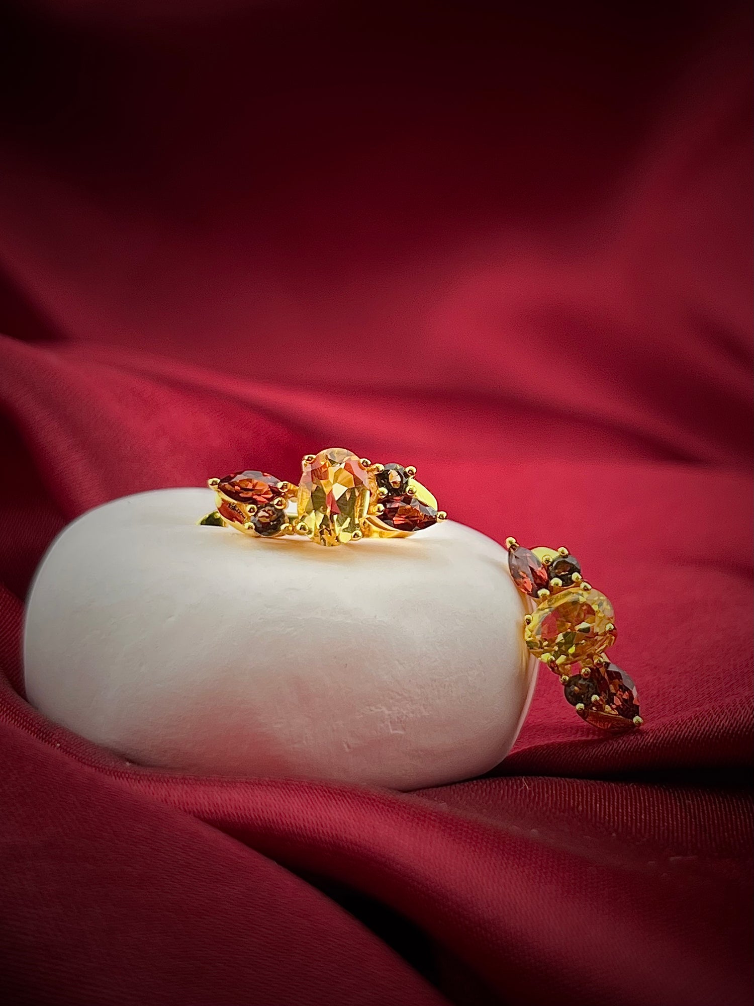 Haspiera harvest hues earrings featuring yellow and red gemstones set in gold on a white display with red fabric background