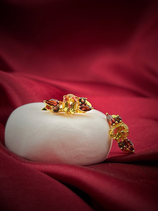 Haspiera harvest hues earrings featuring yellow and red gemstones set in gold on a white display with red fabric background