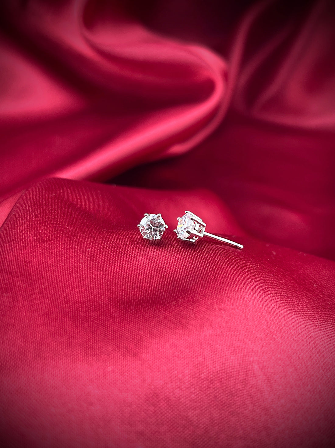 Haspiera lumidot stud earrings with clear gemstone on red satin fabric background