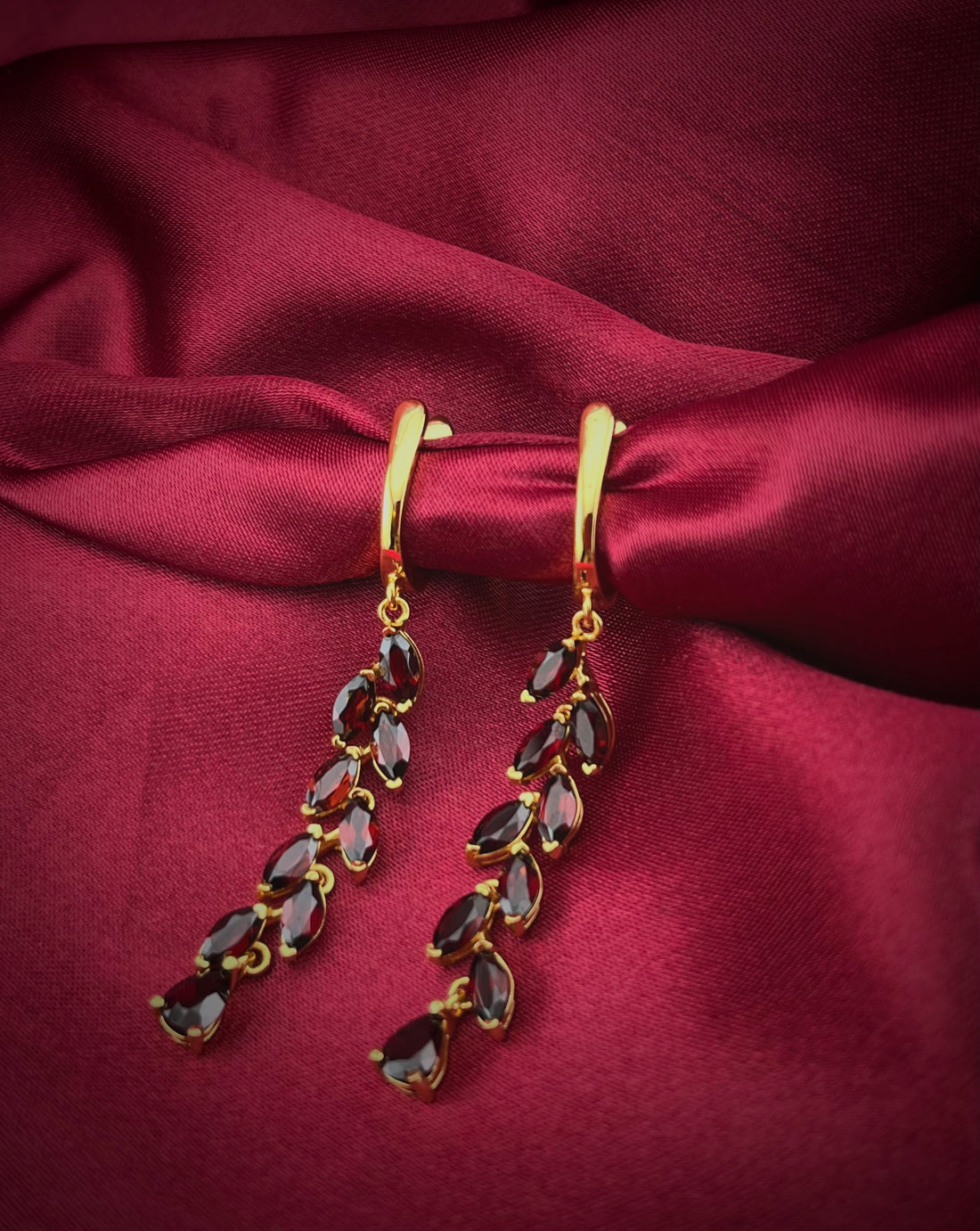 Haspiera elegant red garnet dangle earrings with gold setting displayed on red fabric