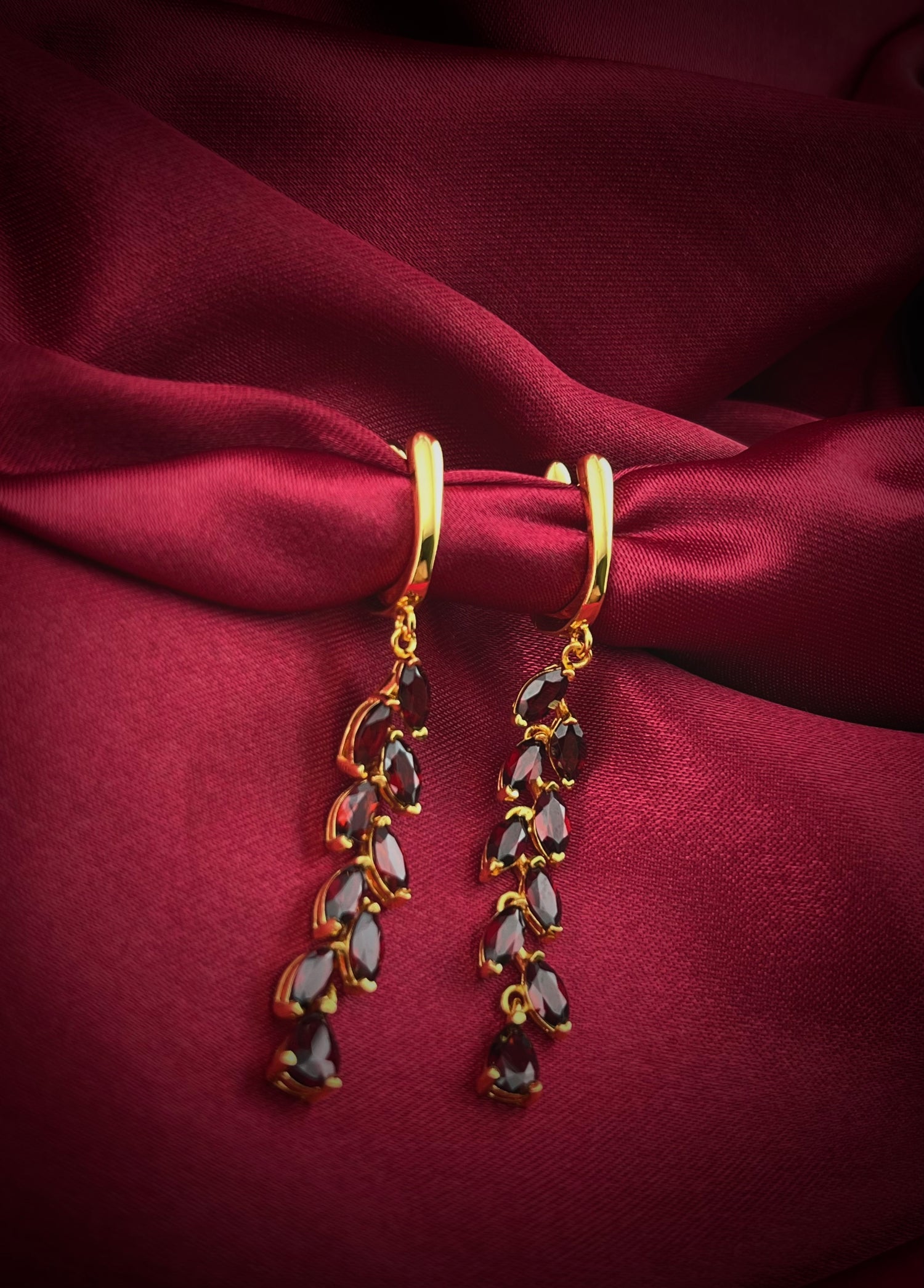Haspiera red garnet dangle earrings with gold settings displayed on red silk fabric