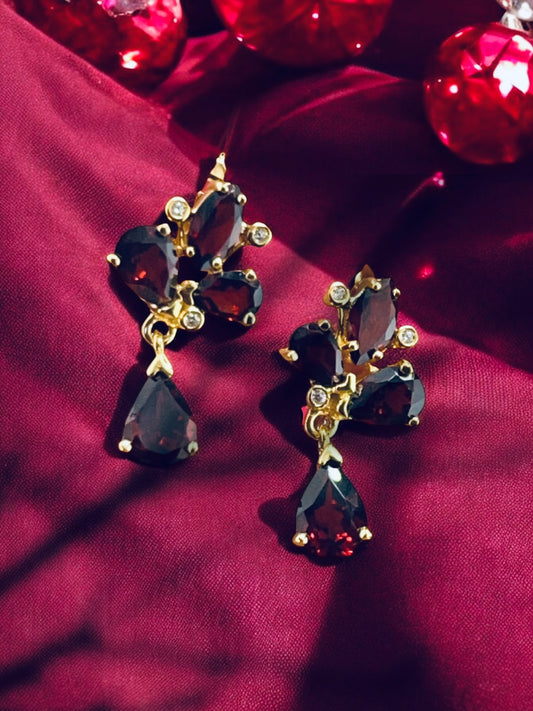 Haspiera red trillium drop earrings with gold setting and deep red gemstones on burgundy fabric