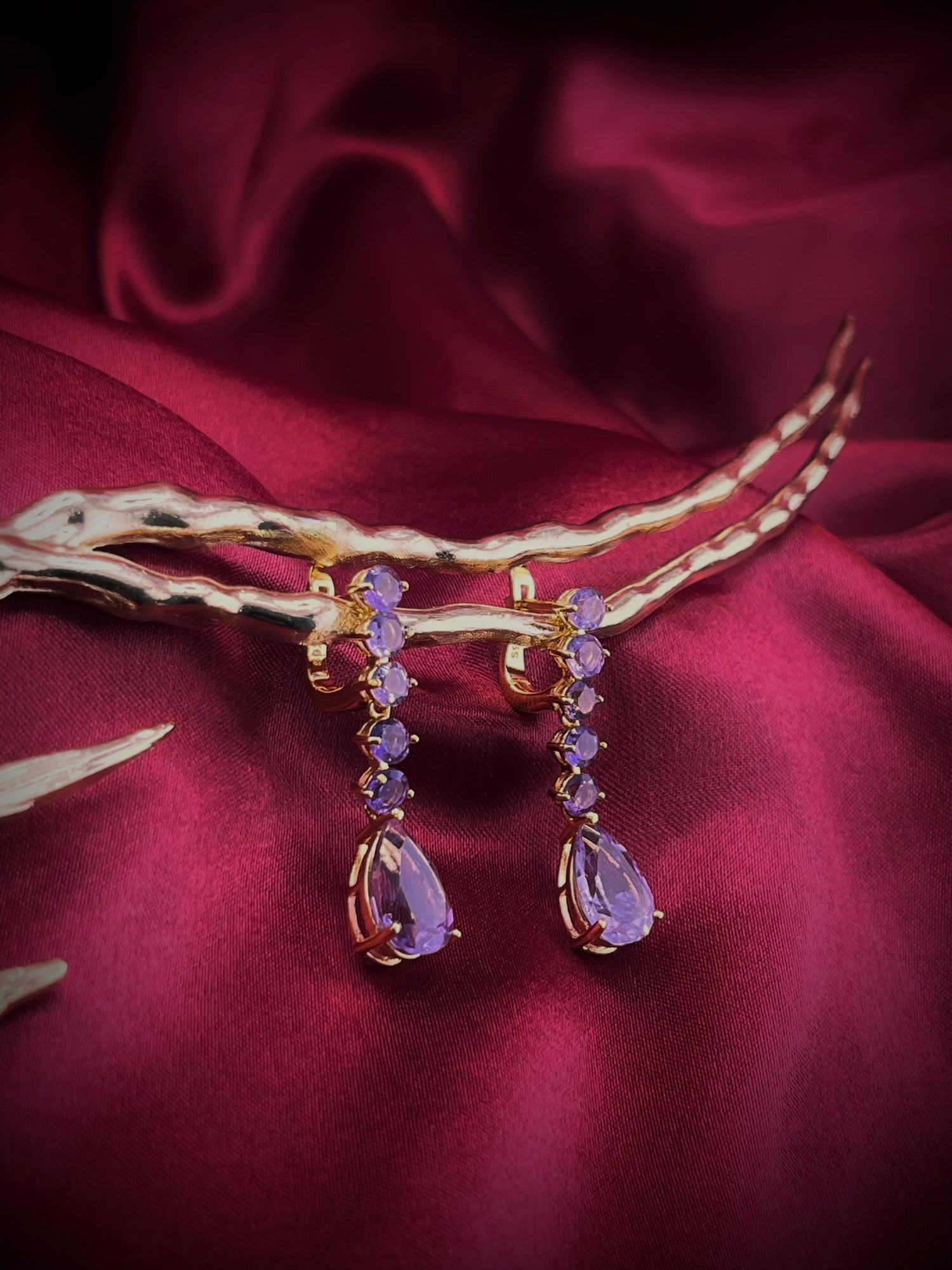 Haspiera royal lilac dangle earrings featuring multiple lilac gemstones set in gold on a red fabric background