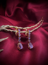 Haspiera royal lilac dangle earrings featuring multiple lilac gemstones set in gold on a red fabric background