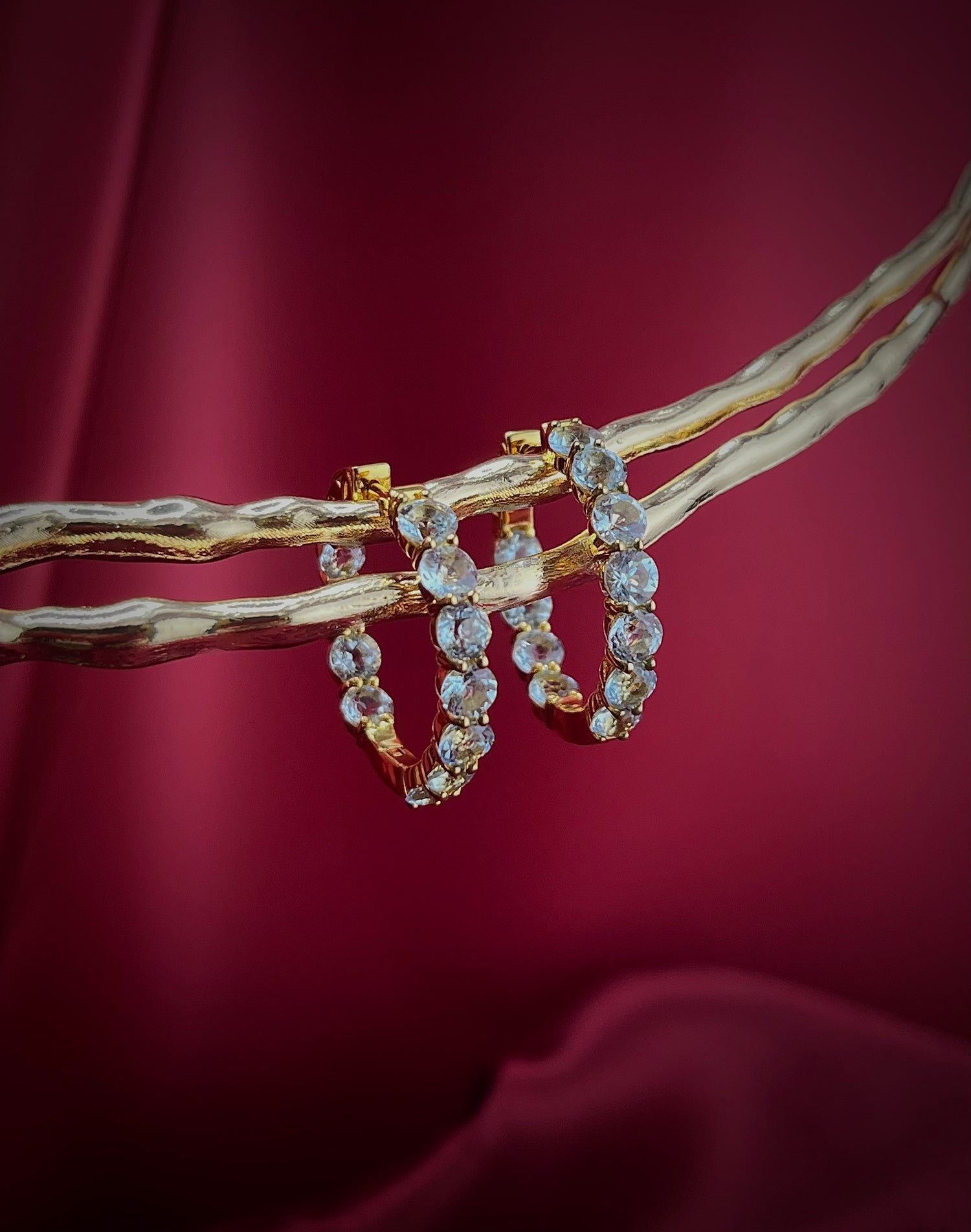 Haspiera sky blue topaz statement hoops earrings with gold setting displayed on branch