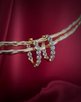 Haspiera sky blue topaz statement hoops earrings with gold setting displayed on branch