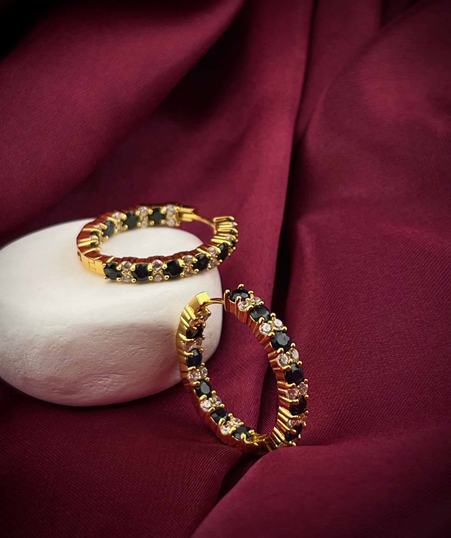 Elegant sapphire and cz hoops gold gemstone earrings by Haspiera displayed on white stone with burgundy fabric background