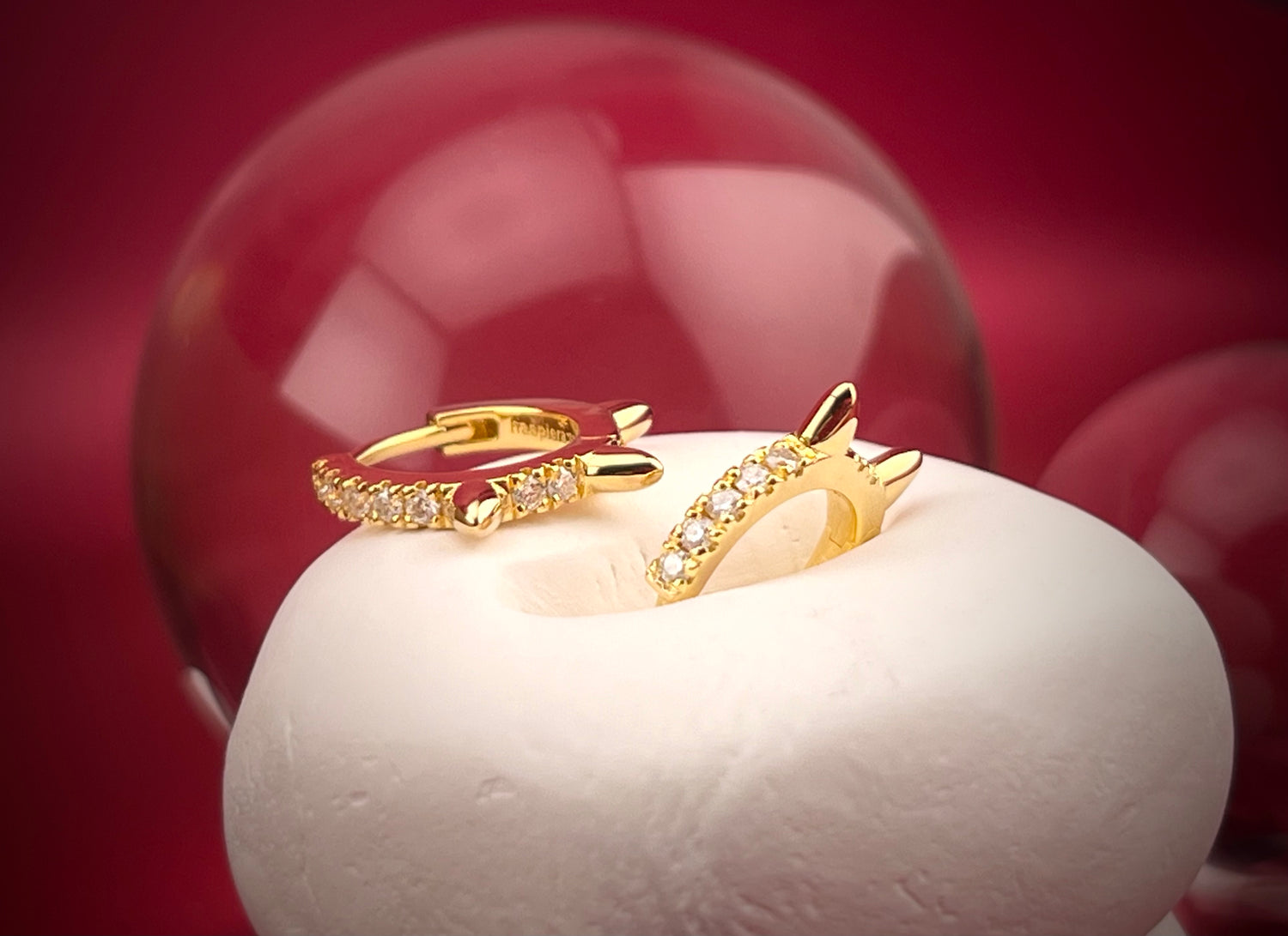 Haspiera gold moissanite spike huggie earrings with sparkling stones on a white display
